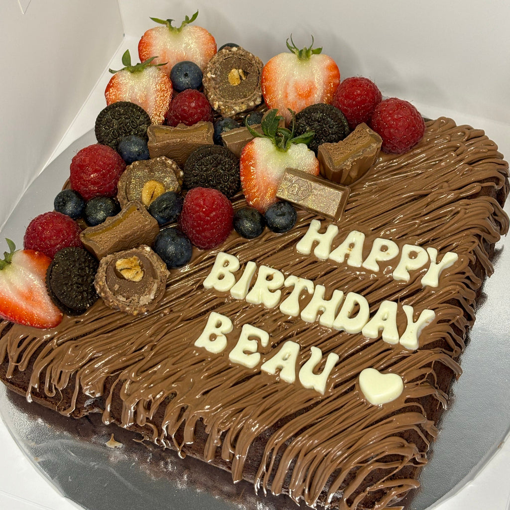 Chocolate birthday brownie slab with berries and chocolate pieces, decorated with 'Happy Birthday Beau' text.