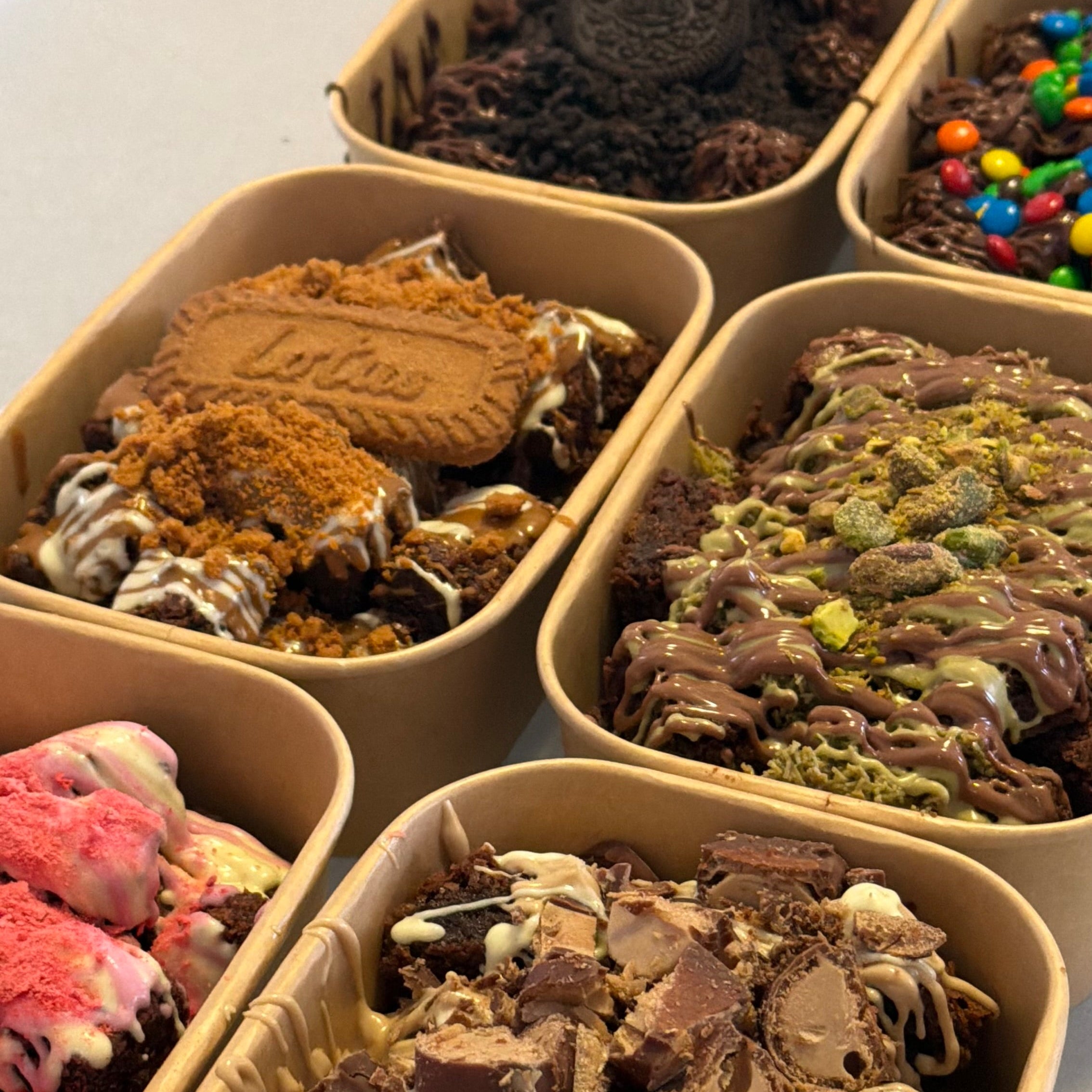 Assorted brownie snack pack treats in small containers on a table. They look delicious.