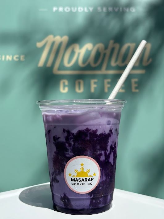 Purple iced drink in a clear cup with a straw, branded 'Moccamain Coffee' and 'Masarap Cookie Co.'