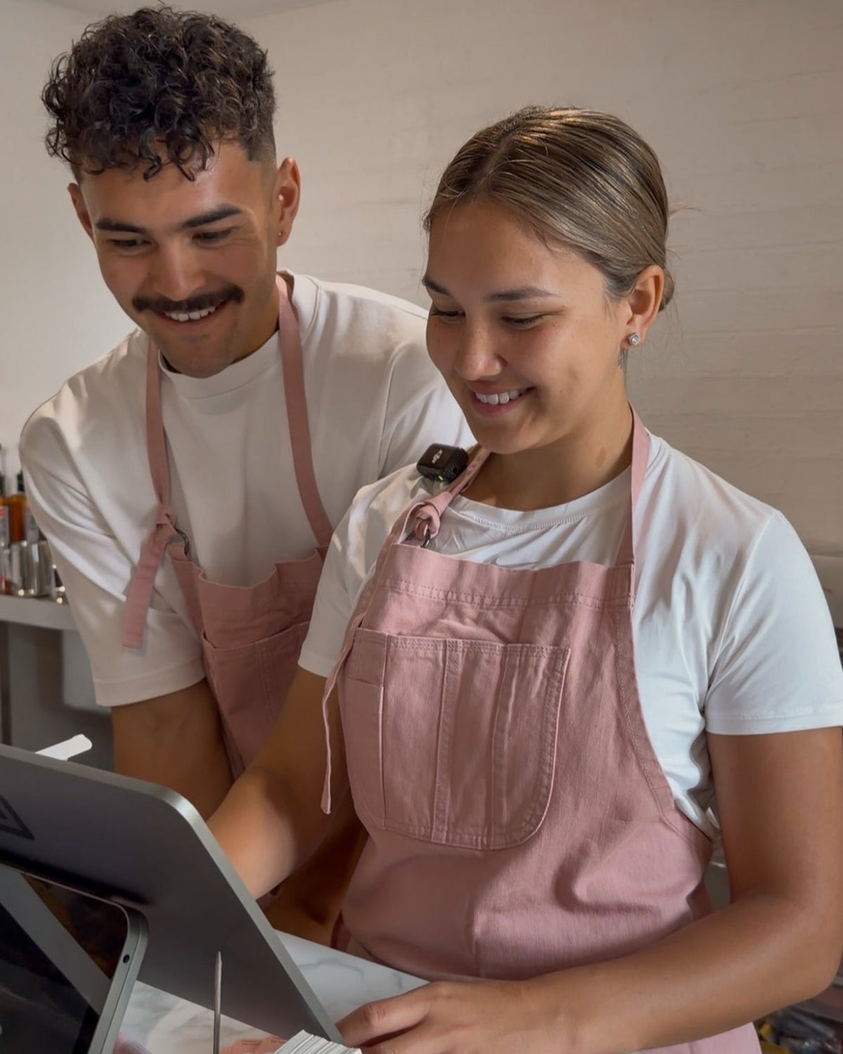 Two people wearing pink aprons working together in a kitchen.