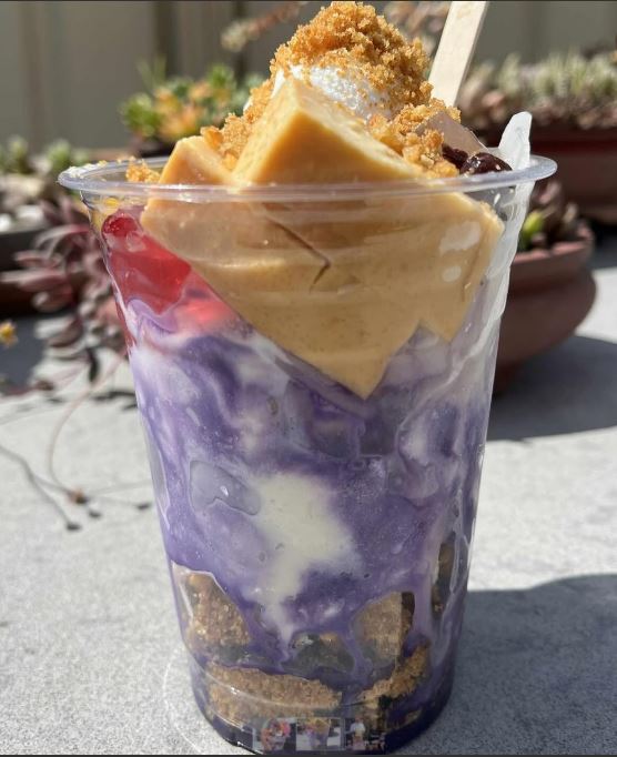 Colorful dessert in a clear cup with a purple swirl, placed outdoors on a concrete surface.